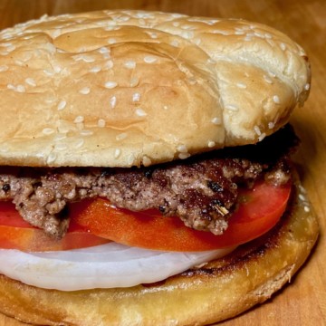 smash burger with tomato and onion on sesame seed bun