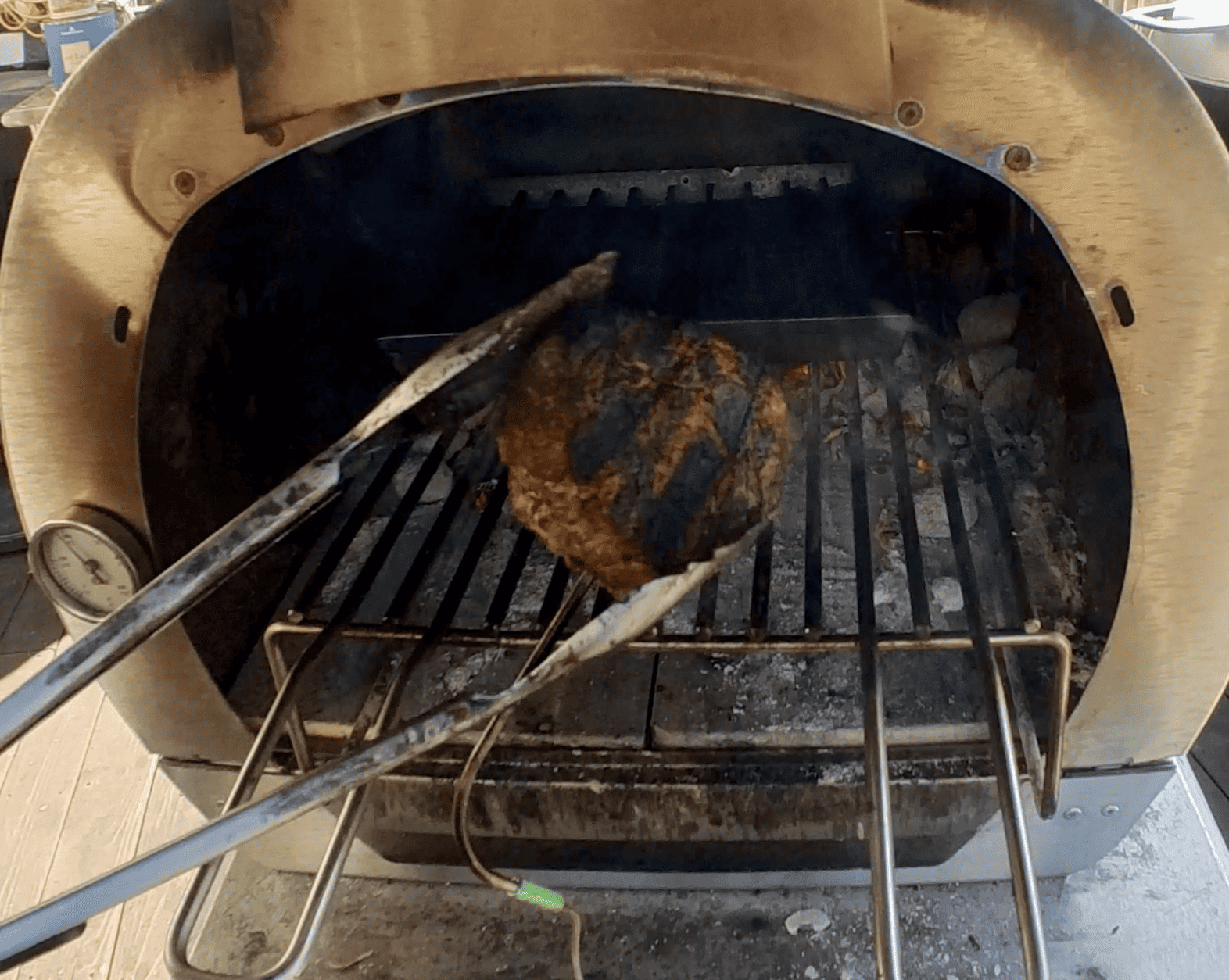 a charred steak with temperature probe cooked in outdoor oven