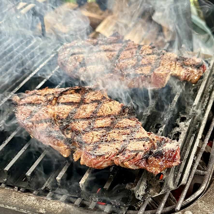Steaks grilling over charcoal with rich sear marks