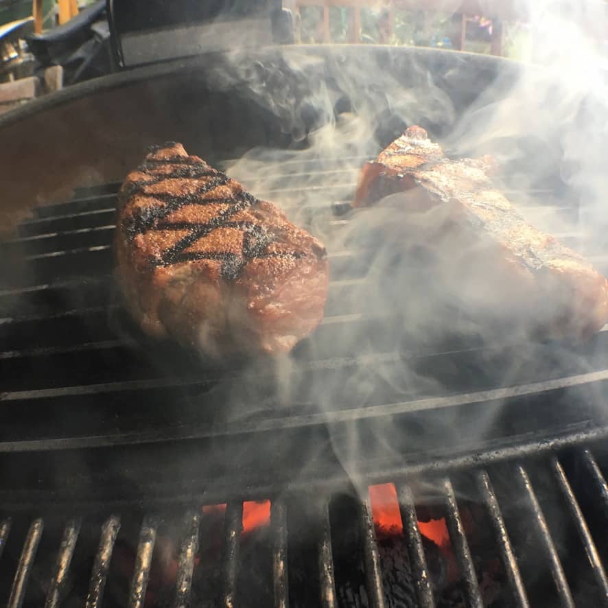 Steaks are cooking on GrillGrates over charcoal