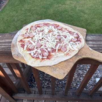 A raw pizza on a pizza peel ready to launch in an outdoor pizza oven.